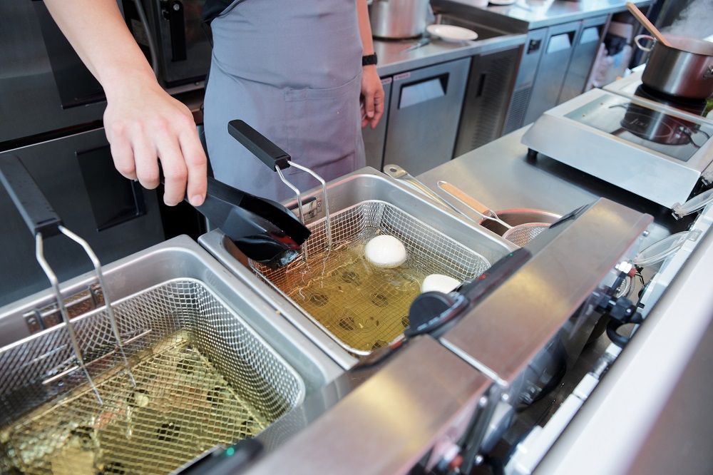 Chef cooking with deep fryer in commercial kitchen